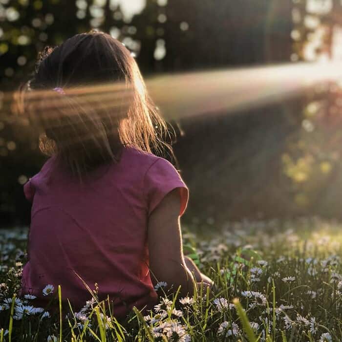 ein Kind sitzt auf einer Blumenwiese und genießt die Sonne