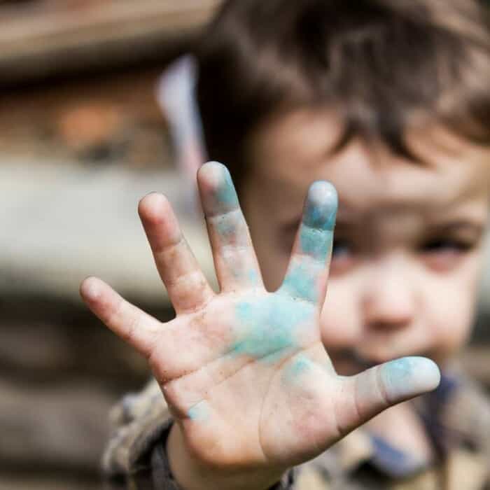 Ein kleiner Junge hält eine Hand in die Kamera. An der Hand ist blaue Farbe.