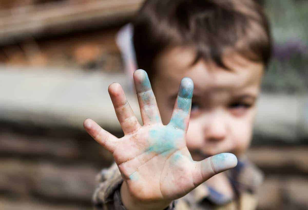 Ein kleiner Junge hält eine Hand in die Kamera. An der Hand ist blaue Farbe.