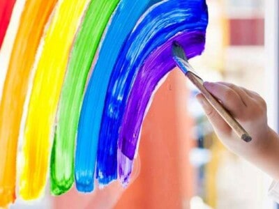 Eine Hand malt mit einem Pinsel einen Regenbogen an das Glas.