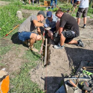 Mehrere Personen arbeiten in einem Garten. Drei Männer verlegen ein Rohr im Boden.