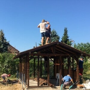 Mehrere Personen arbeiten an einem Haus aus Holz. Auf dem Dach stehen ebenfalls zwei Männer.