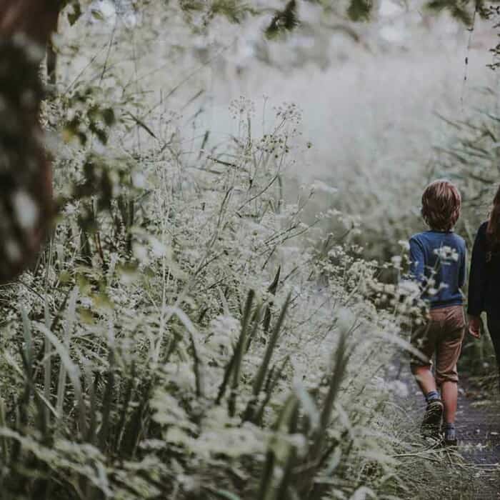 Ein Junge und ein Mädchen laufen auf einem Weg. Am Wegrand wächst Gras und hohe Sträucher.
