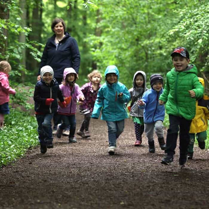 Viele Kinder laufen auf einem Waldweg. Hinter den Kindern steht eine Pädagogin.