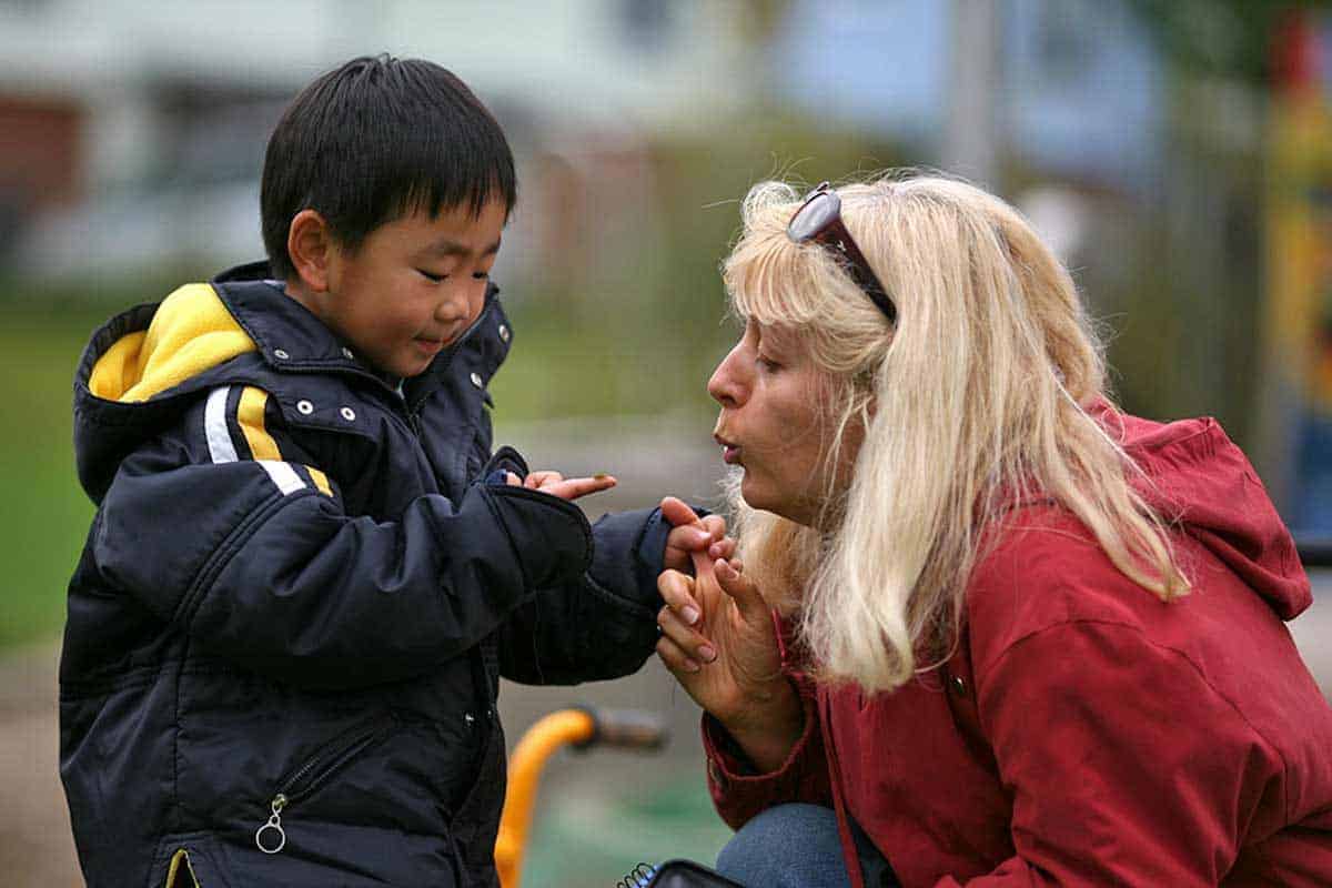 blonde Pädagogin pustet kleinem Jungen auf den Finger, auf dem ein Marienkäfer sitzt