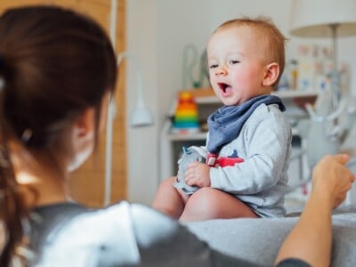 Ein Kleinkind nutzt die Mundmotorik, um mit einer ihm gegenübersitzenden Frau zu kommunzieren.