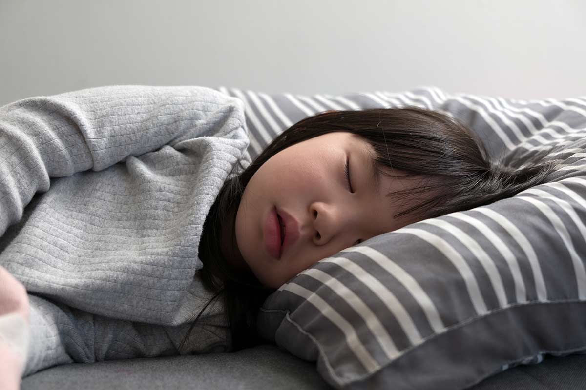Ein Mädchen liegt mit dem Kopf auf einem Kissen und hat die Augen geschlossen.