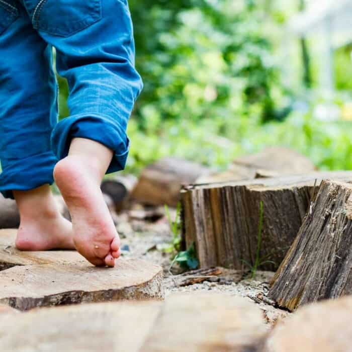 Ein Kind läuft barfuß auf hölzernen Untergrund in der Natur.
