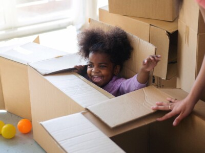 Ein Kind spielt sitzend in einem Karton und freut sich.
