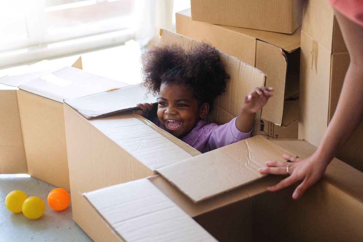 Ein Kind spielt sitzend in einem Karton und freut sich.