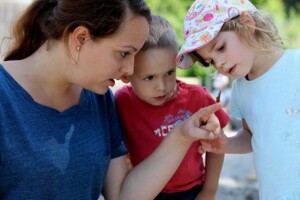 Zwei Kinder und eine Frau beobachten einen Schmetterling, der sich auf den Zeigefinger der Frau gesetzt hat.