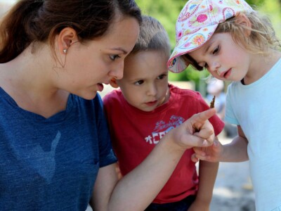 Zwei Kinder und eine Frau beobachten einen Schmetterling, der sich auf den Zeigefinger der Frau gesetzt hat.