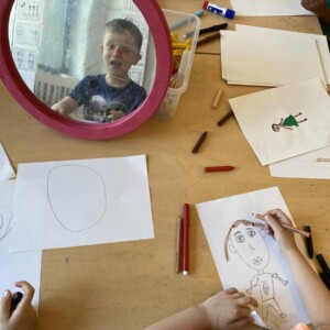 Ein Junge betrachtet sich im Spiegel und malt zugleich sein Selbstportrait.