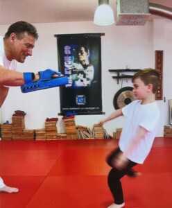 Kitakind übt Tritte an einem Polster, das vom Judolehrer gehalten wird
