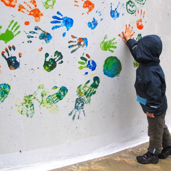 Ein Kind macht Handabdrücke in verschiedenen Farben auf eine weiße Wand.
