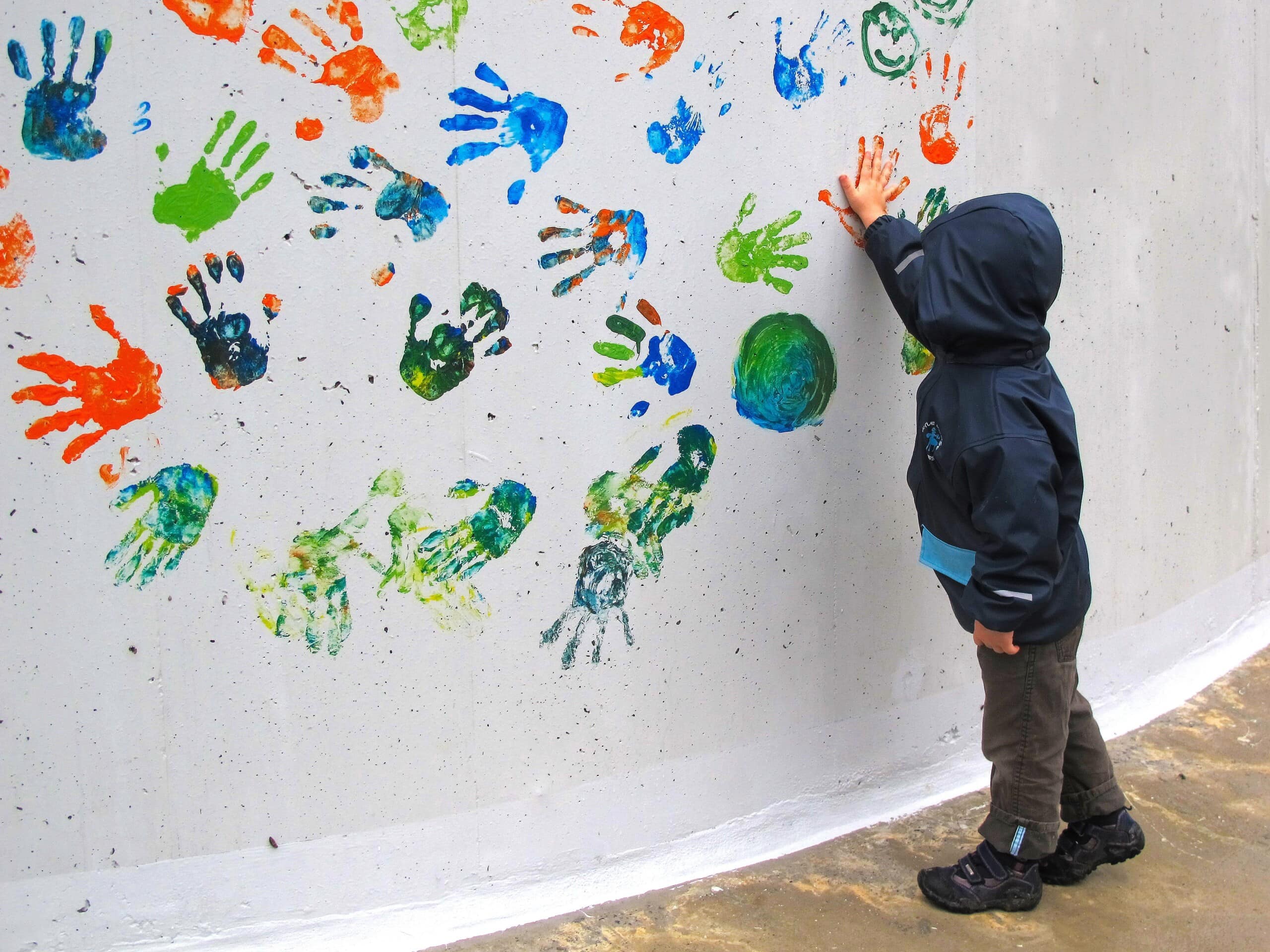 Ein Kind macht Handabdrücke in verschiedenen Farben auf eine weiße Wand.