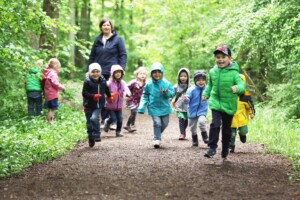 Kinder in bunten Jacken rennen durch den Wald.