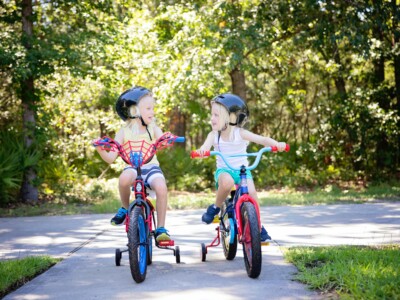 zwei blonde Mädchen auf Fahrrädern mit Stützrädern schauen sich lachend an