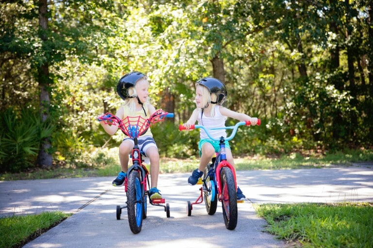 zwei blonde Mädchen auf Fahrrädern mit Stützrädern schauen sich lachend an