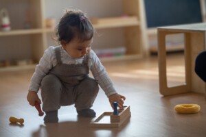 Ein Kind ist in einem Gruppenraum und spielt mit einem Holzspielzeug.
