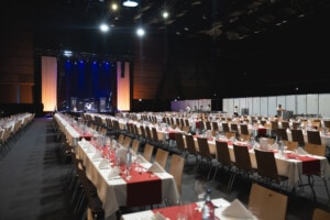 Großer Saal mit langen, gedeckten Tischen und einer Bühne