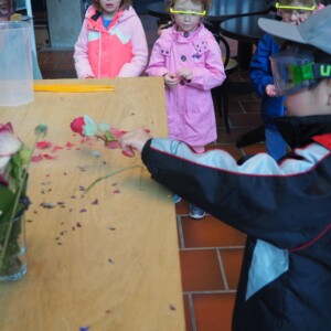 Kinder stehen mit Schutzbrillen an einem Tisch und forschen gemeinsam.