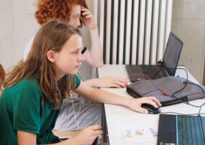 Eine Schülerin und ein Schüler sitzen an ihren Laptops und arbeiten.