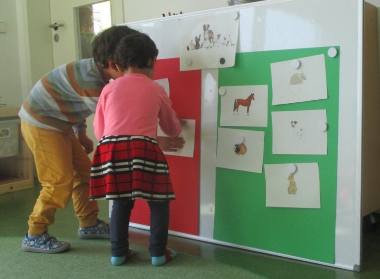 Zwei Kinder hängen gemalte Bilder von Tieren an eine Tafel.