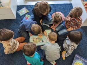 Mehrere Kinder betrachten gemeinsam mit einer Frau eine Weltkarte in einem Buch.