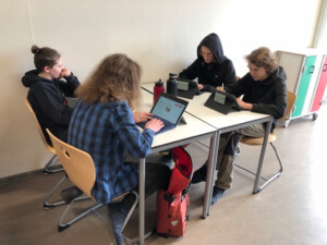 Schüler sitzen an einem Vierer-Tisch und arbeiten an ihren Laptops.