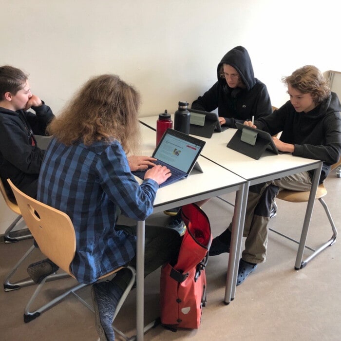Schüler sitzen an einem Vierer-Tisch und arbeiten an ihren Laptops.